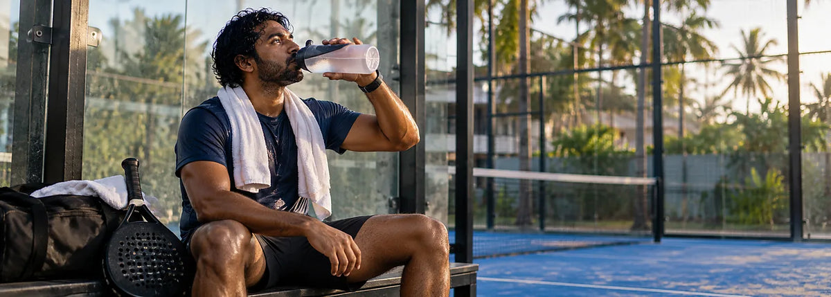 South Asian padel player hydrating between matches in warm tropical conditions